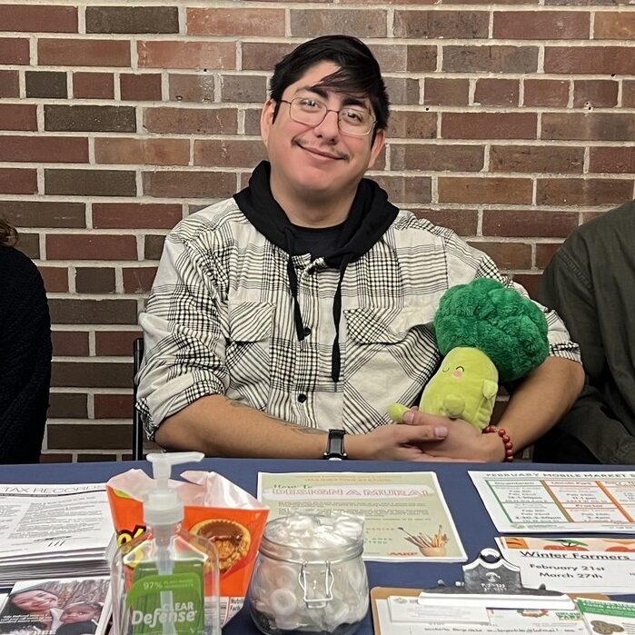 Three smiling people sit behind a table with lots of papers and information.