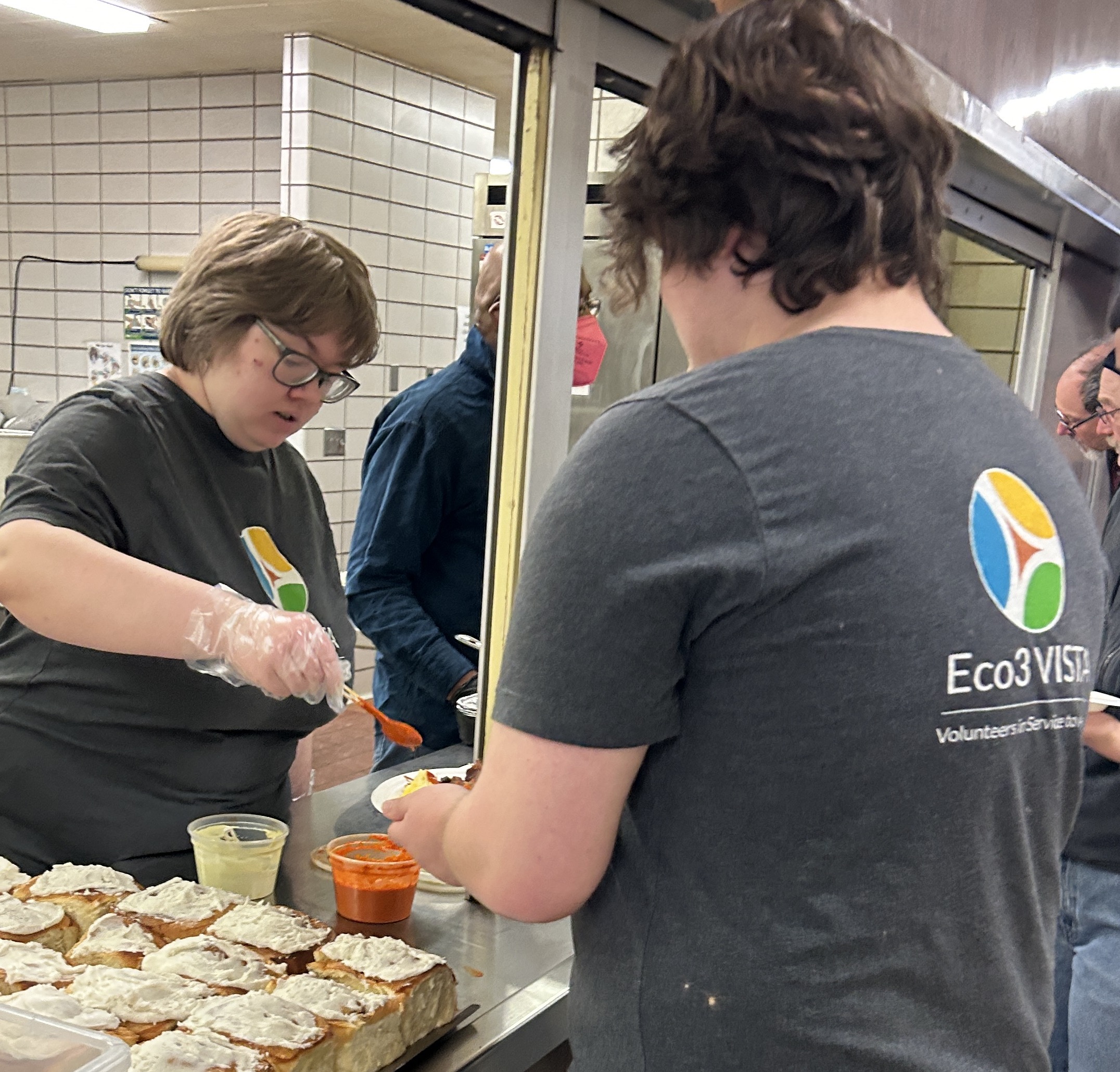 Person spoons food onto another person's plate. They are both wearing Eco3 VISTA shirts.