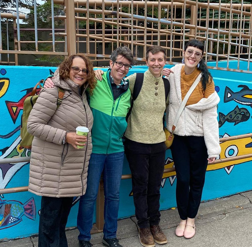 Four smiling people pose in front of a colorful mural.