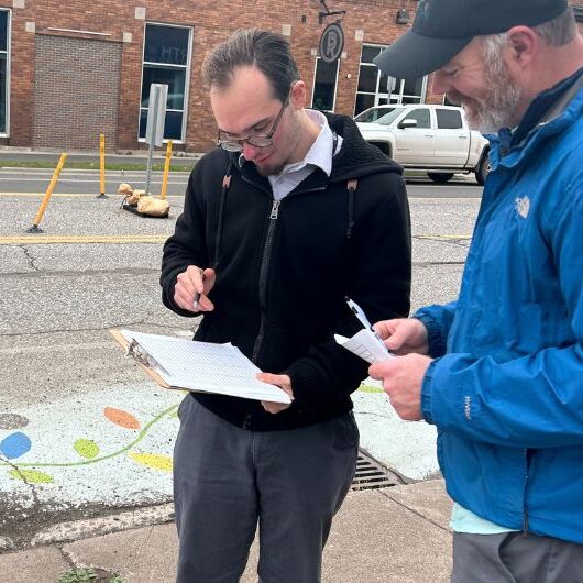 Two people look at a clipboard near a crosswalk.