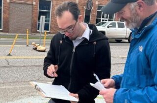 Two people look at a clipboard near a crosswalk.