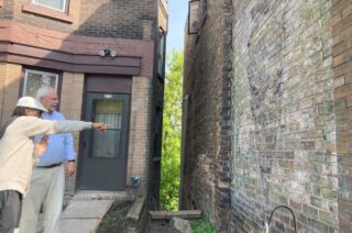 Two people point at a brick building and talk.