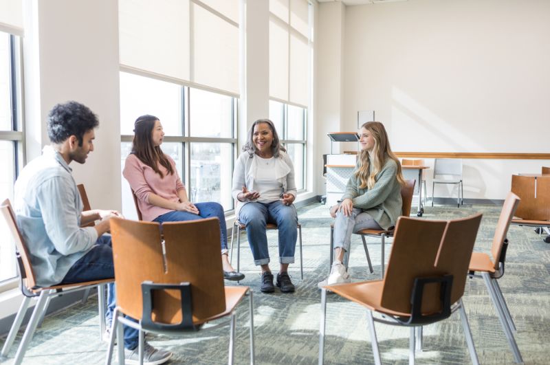 Stock image of four people sitting in chairs and talking.